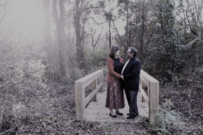 couple standing hand in hand on footbridge, looking lovingly at each other